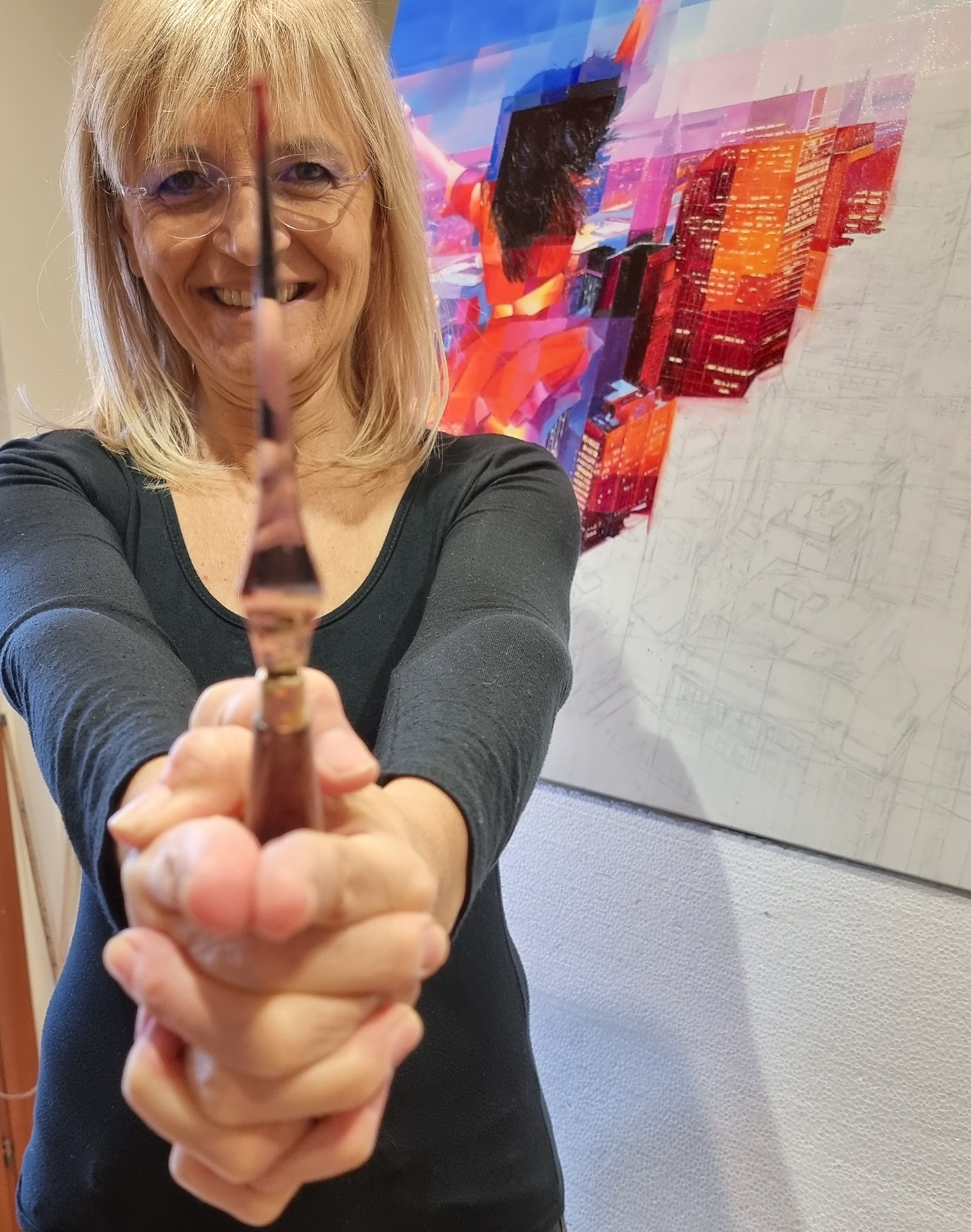 A smiling artist holding a palette knife towards the camera, creating a striking visual effect. Behind her, a vibrant urban-inspired painting featuring a dynamic figure in red emerges on the canvas. The image captures the artist’s passion and playfulness, highlighting the importance of the palette knife in her technique.