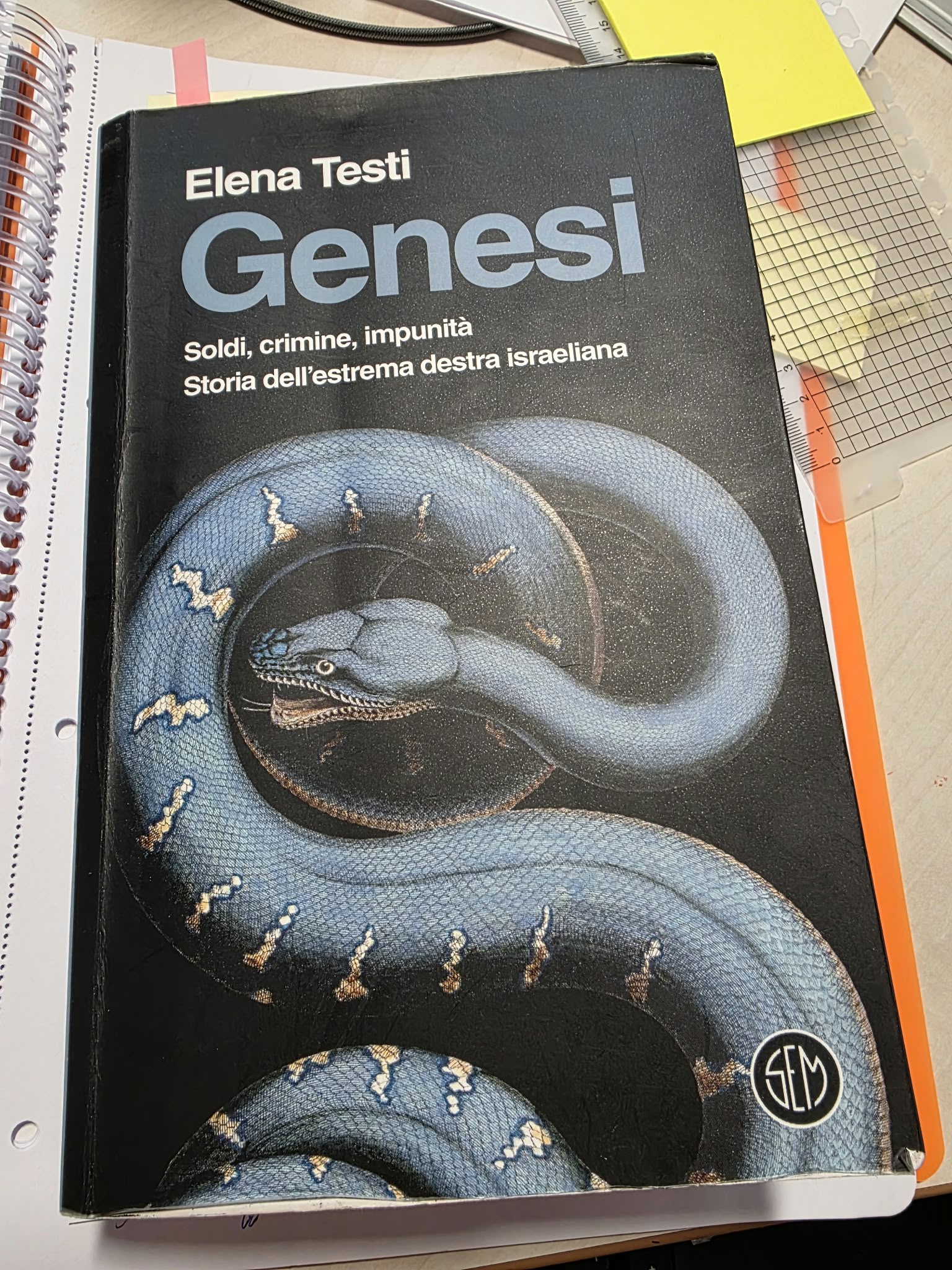 Elena Testi’s book Genesi, marked with notes and tabs, on Assunta Cassa’s desk while she prepares for the author event.